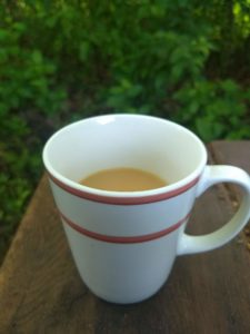 white mug with pink lines with coffee on a table outside.