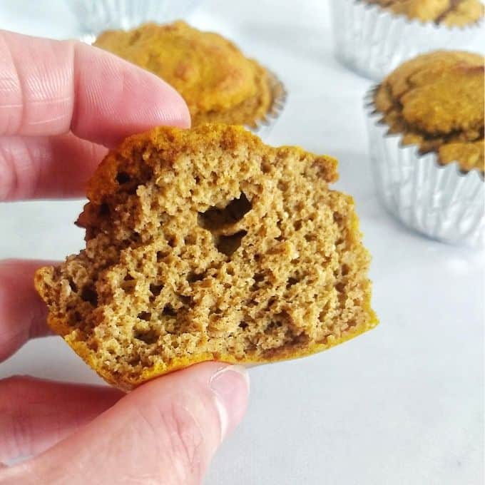 A hand holding a pumpkin muffin with an inside bite