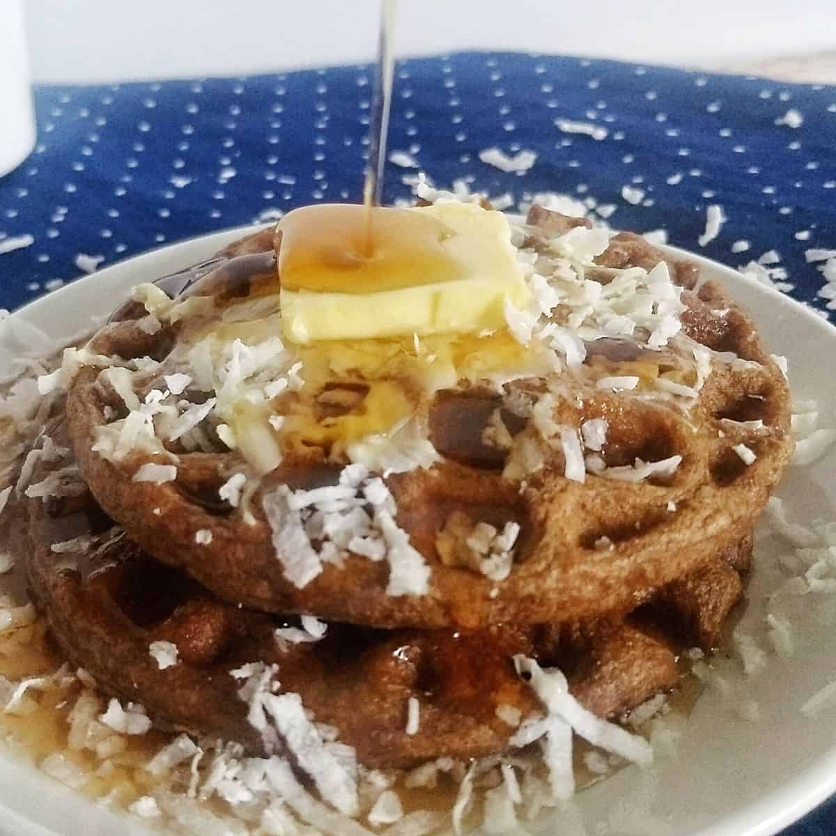 2 chocolate waffles stacked with butter, coconut flakes and syrup