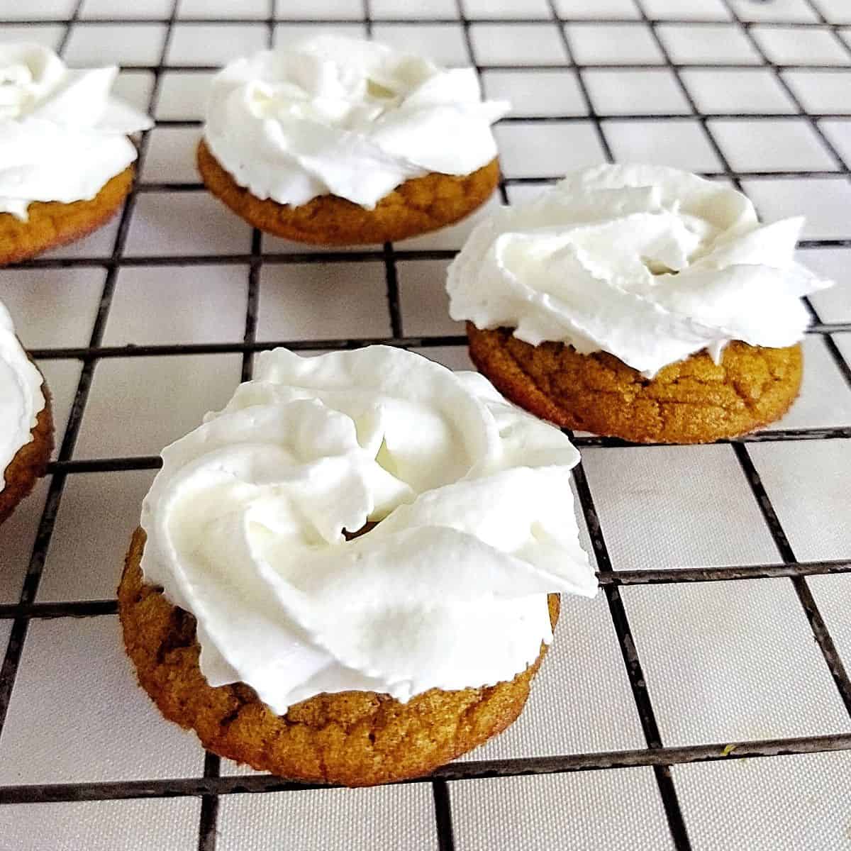 pumpkin cookies with whipped cream on top on top of a cooling rack.