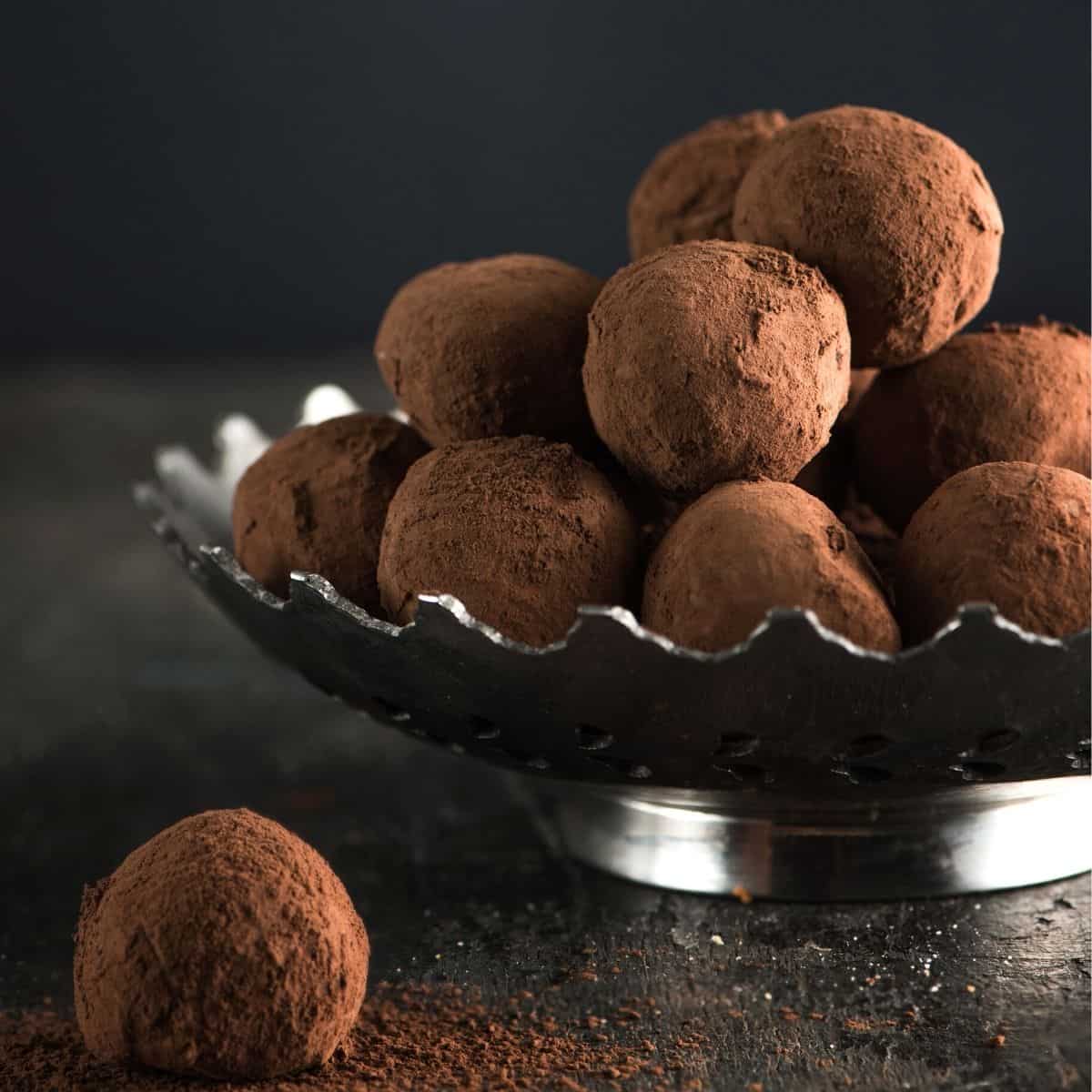 Chocolate truffles in a silver bowl with 1 sitting on the table