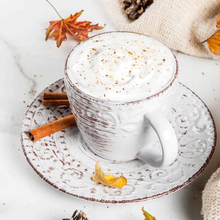 coffee in a white and brown cup with leaves and cinnamon sticks