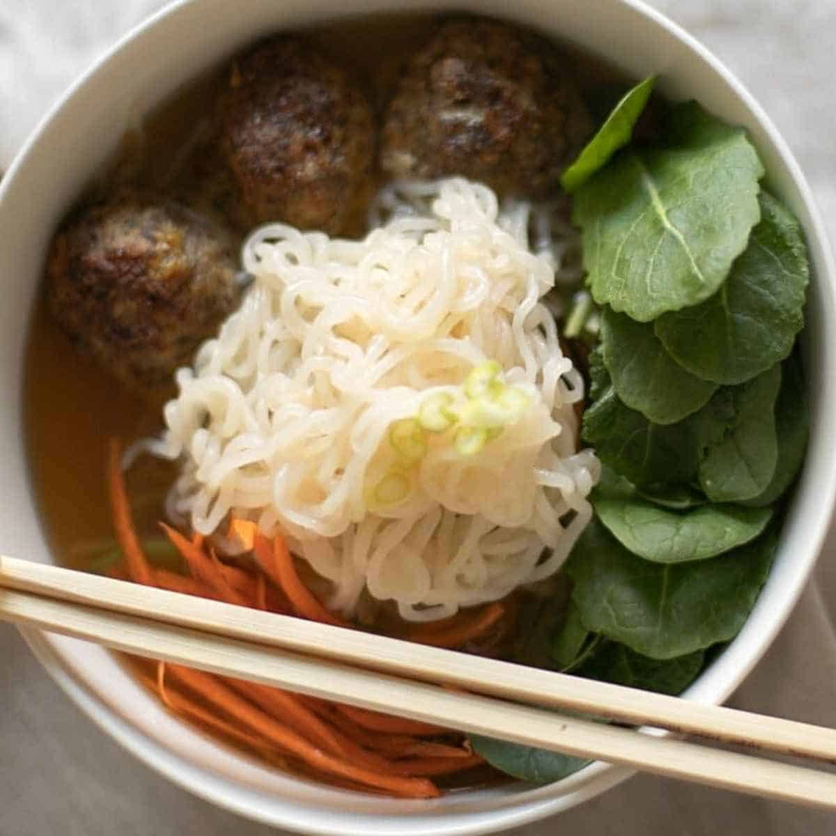 Meatballs, noodles, green leaves and carrots in a bowl for soup.