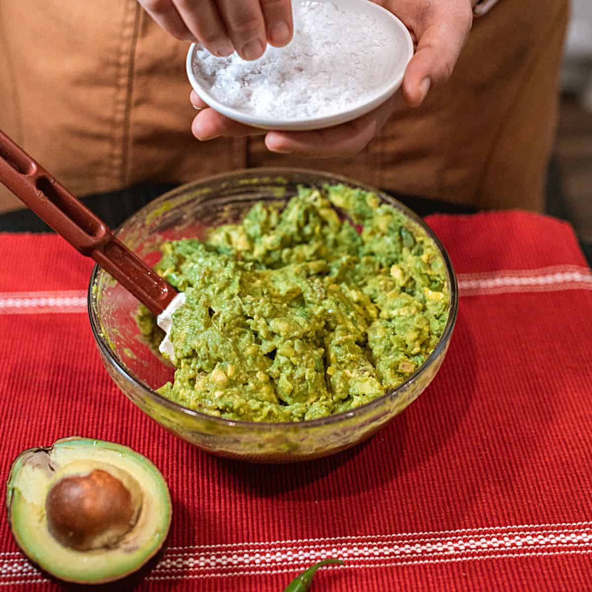 bowl of guac getting salt mixed in - Guacamole is keto & Here's Why with Recipes