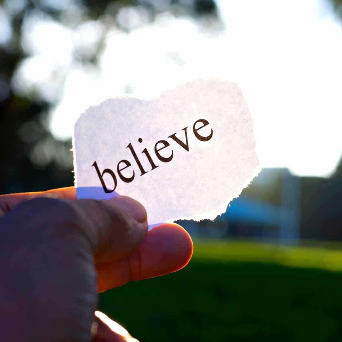 a hand holding a piece of paper with the word believe on it