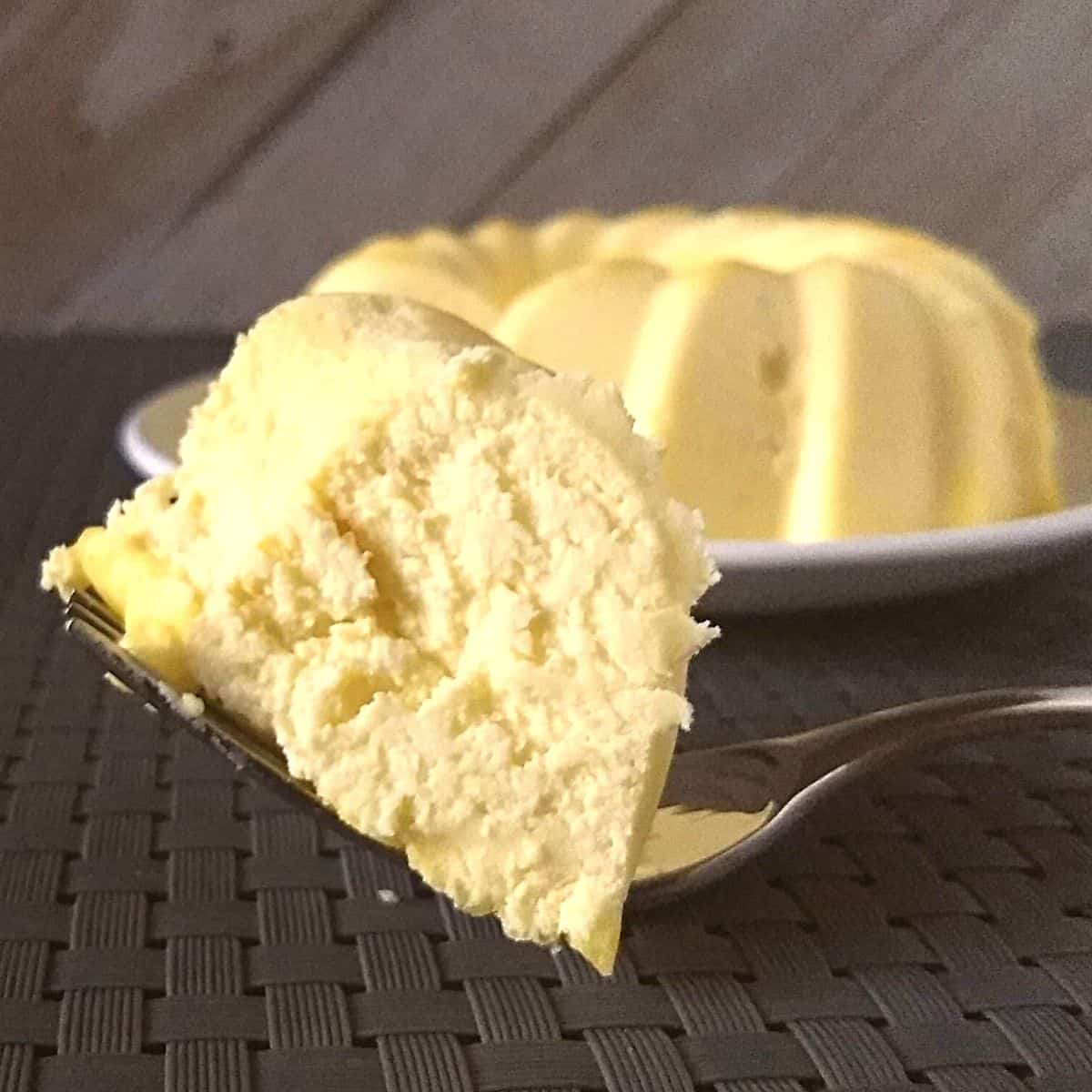 Piece of lemon cake on a fork in front o the whole cake